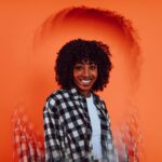 Portrait-of-a-woman-with-curly-hair-and-checkered-shirt-against-an-artistic-orange-backdrop.-2025-05-23T060323.719-0400-pexels-photo-6923254