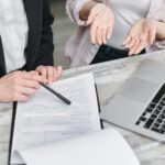 Two-professionals-discussing-a-contract-at-a-business-meeting-with-documents-and-a-laptop.-2025-05-23T153708.475-0400-pexels-photo-7731402