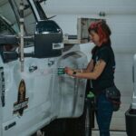Woman-applying-a-safety-sticker-on-a-truck-in-an-indoor-garage-setting-Calgary-Canada.-2025-05-25T060321.603-0400-pexels-photo-15549935